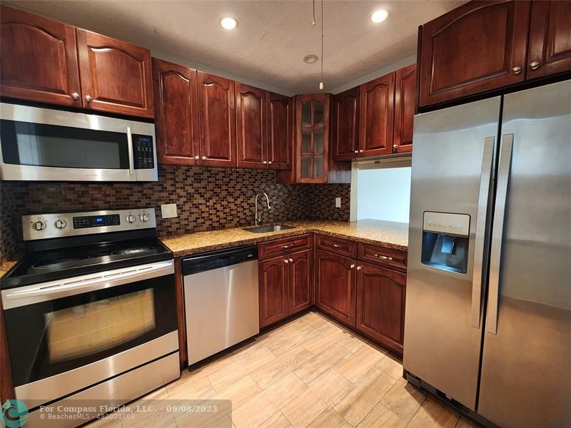 a kitchen with stainless steel appliances granite countertop wooden cabinets a stove a sink and a microwave