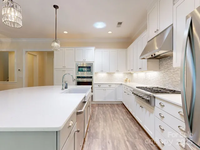 a large kitchen with stainless steel appliances a stove a sink dishwasher and a refrigerator with wooden floor