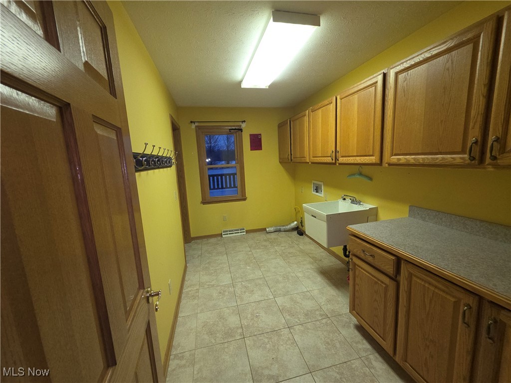2291 Armstrong Road Wooster, OH 44691 - Photo 13 of 23 Laundry room with washer hookup, gas or electric dryer hookup, a textured ceiling, cabinet space, and light tile patterned flooring