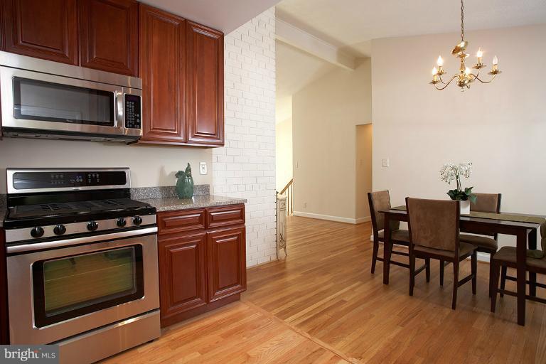 11204 Monticello Avenue Silver Spring, MD 20902 - Photo 27 of 29 a kitchen with stainless steel appliances a stove a microwave a dining table and chairs with wooden floor
