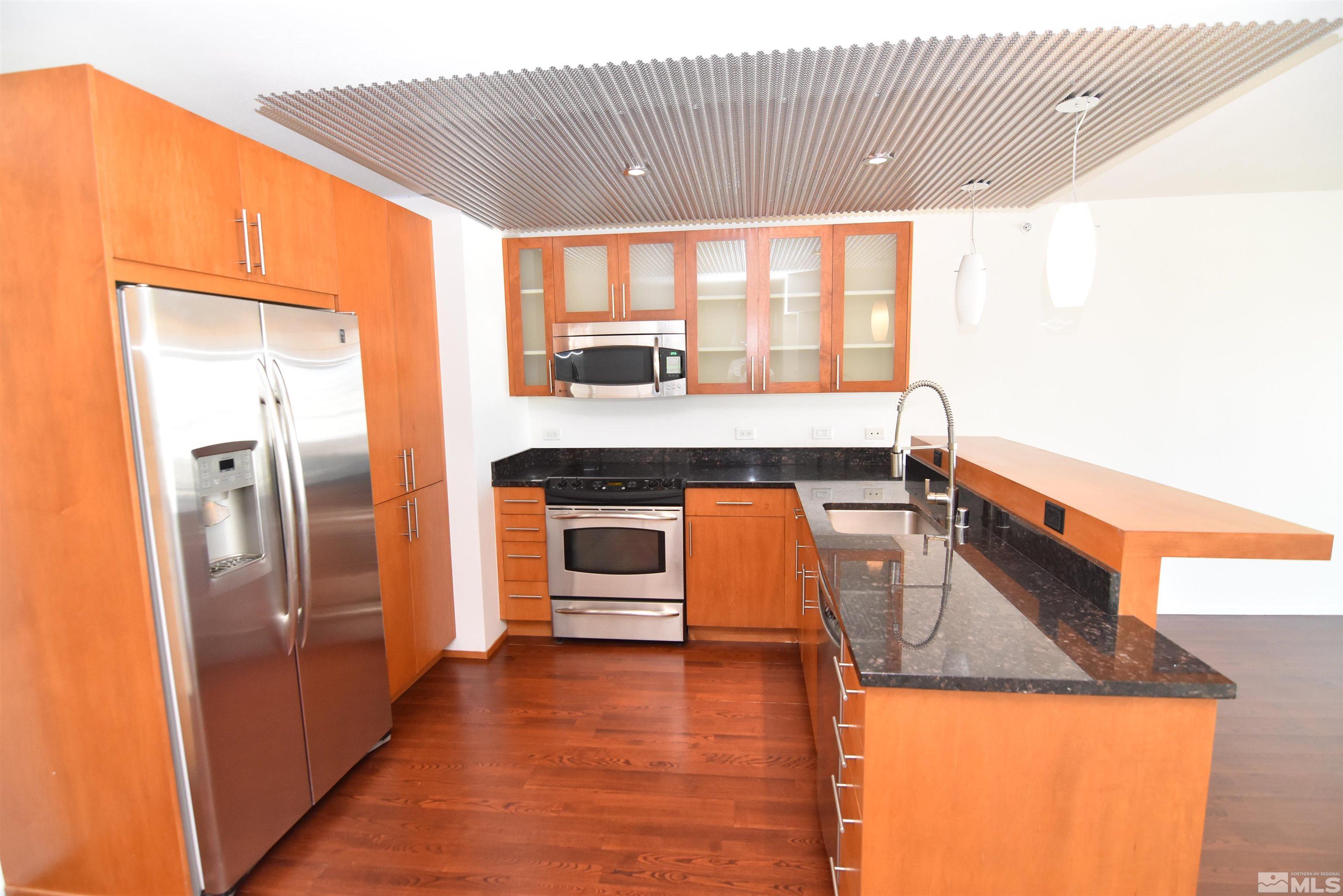 a kitchen with stainless steel appliances granite countertop a refrigerator a stove and a wooden floor