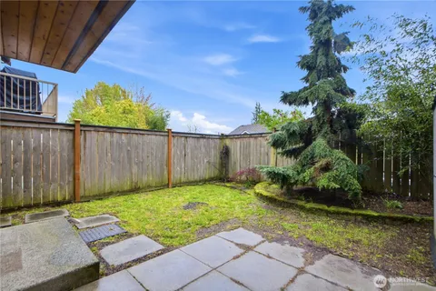 a view of a backyard with plants and large trees with wooden fence