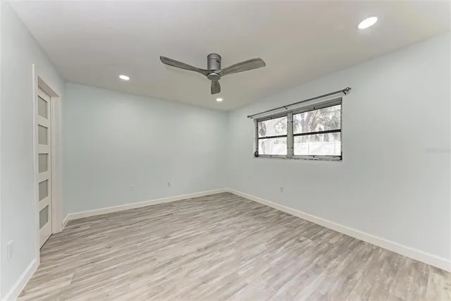 an empty room with wooden floor ceiling fan and windows