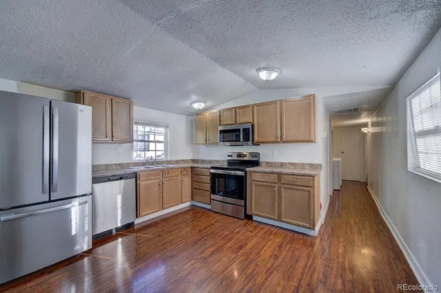 a kitchen with granite countertop stainless steel appliances a refrigerator cabinets and wooden floor