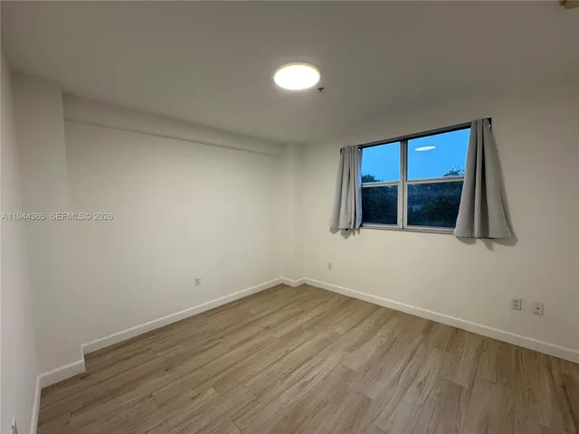 a view of an empty room with wooden floor and fan