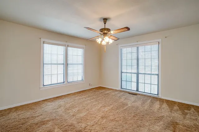 an empty room with chandelier fan and windows