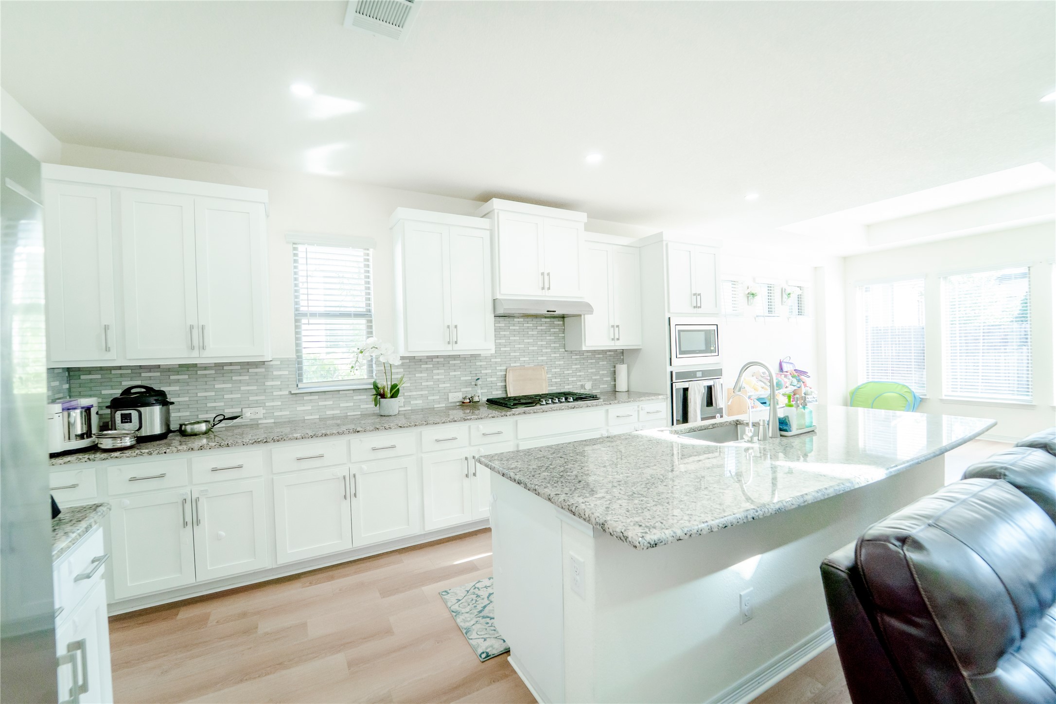 20813 Carries Ranch Road Pflugerville, TX 78660 - Photo 9 of 29 Kitchen with light stone countertops, light wood-type flooring, white cabinets, a center island with sink, and recessed lighting