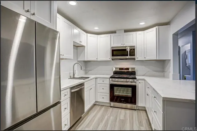 a kitchen with stainless steel appliances granite countertop white cabinets a sink a stove a refrigerator and a oven with wooden floor