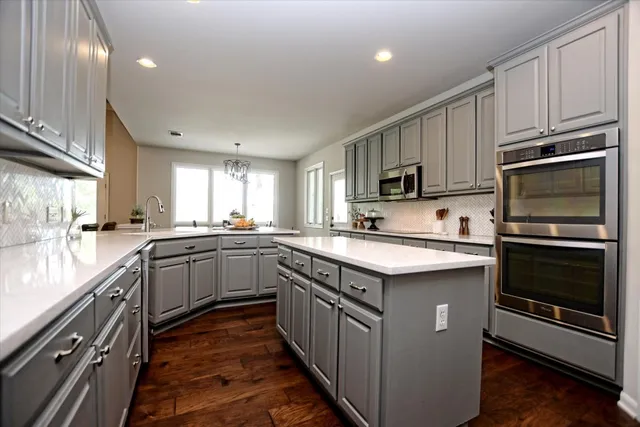 a kitchen with stainless steel appliances granite countertop a stove top oven a sink dishwasher a refrigerator and a microwave oven with wooden floor