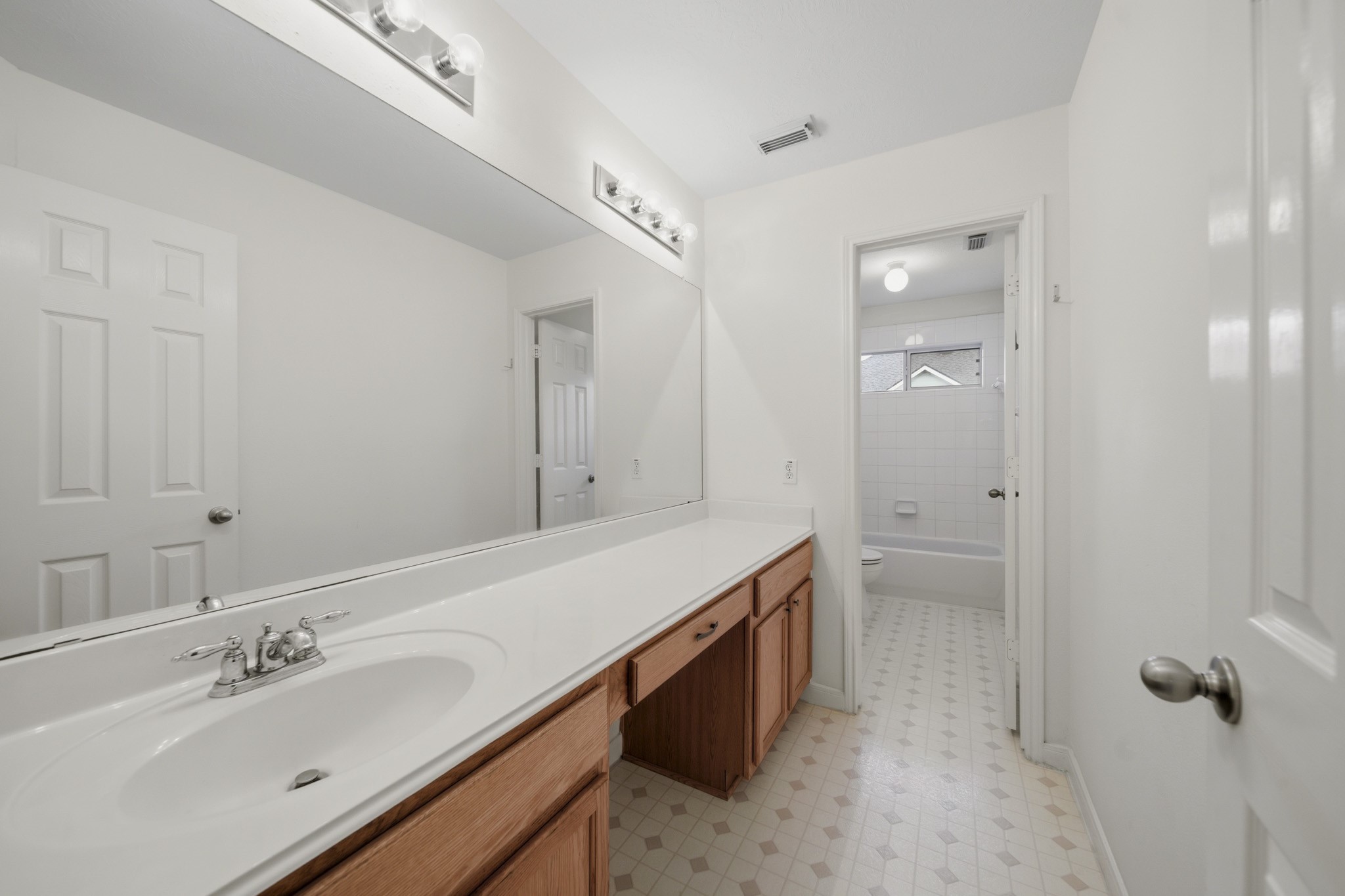 3306 Colleville Sur Mer Lane Spring, TX 77388 - Photo 19 of 30 This spacious secondary bathroom is designed with both functionality and convenience in mind. The oversized vanity offers abundant countertop space and storage, making it ideal for busy mornings and shared use. A large wall-to-wall mirror enhances the sense of space while reflecting light throughout the room. The bathroom features a separate tub and shower area, providing privacy and flexibility for daily routines.