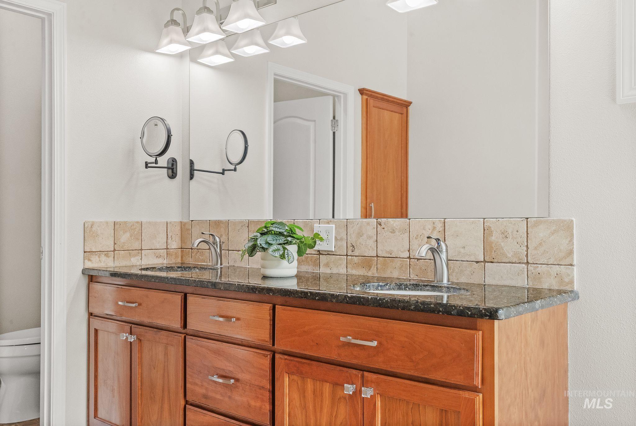 602 Quarry Road Asotin, WA 99402 - Photo 26 of 49 Double vanity featuring wood cabinetry, dark speckled countertop, undermount sinks with chrome faucets, and a tiled backsplash