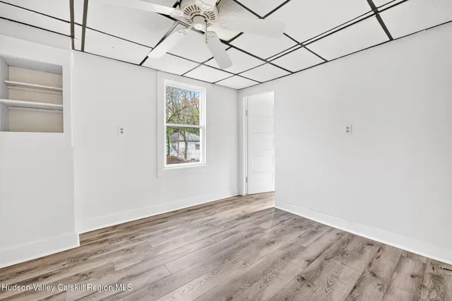 an empty room with wooden floor chandelier fan and windows