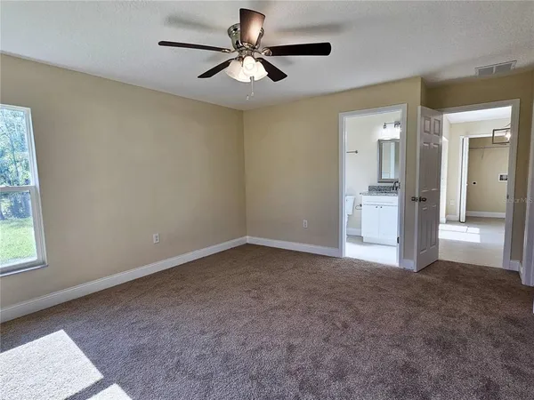 an empty room with chandelier fan and windows