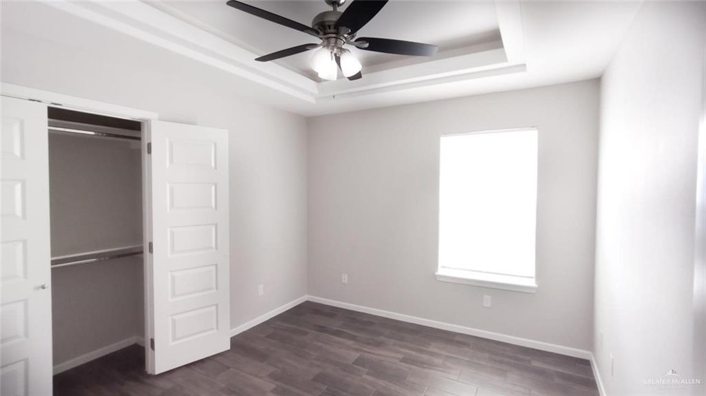 701 Cathedral Hill, Unit 1 Edinburg, TX 78541 - Photo 6 of 14 Unfurnished bedroom with dark wood-style flooring, a tray ceiling, a ceiling fan, and a closet