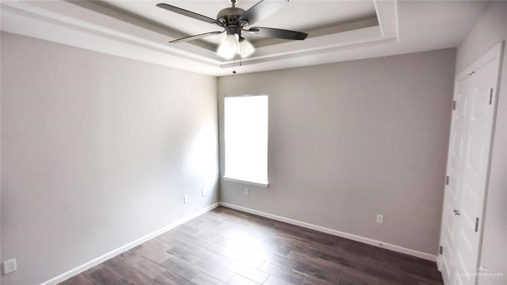 701 Cathedral Hill, Unit 1 Edinburg, TX 78541 - Photo 9 of 14 Unfurnished bedroom featuring dark wood-style flooring, a tray ceiling, and a ceiling fan