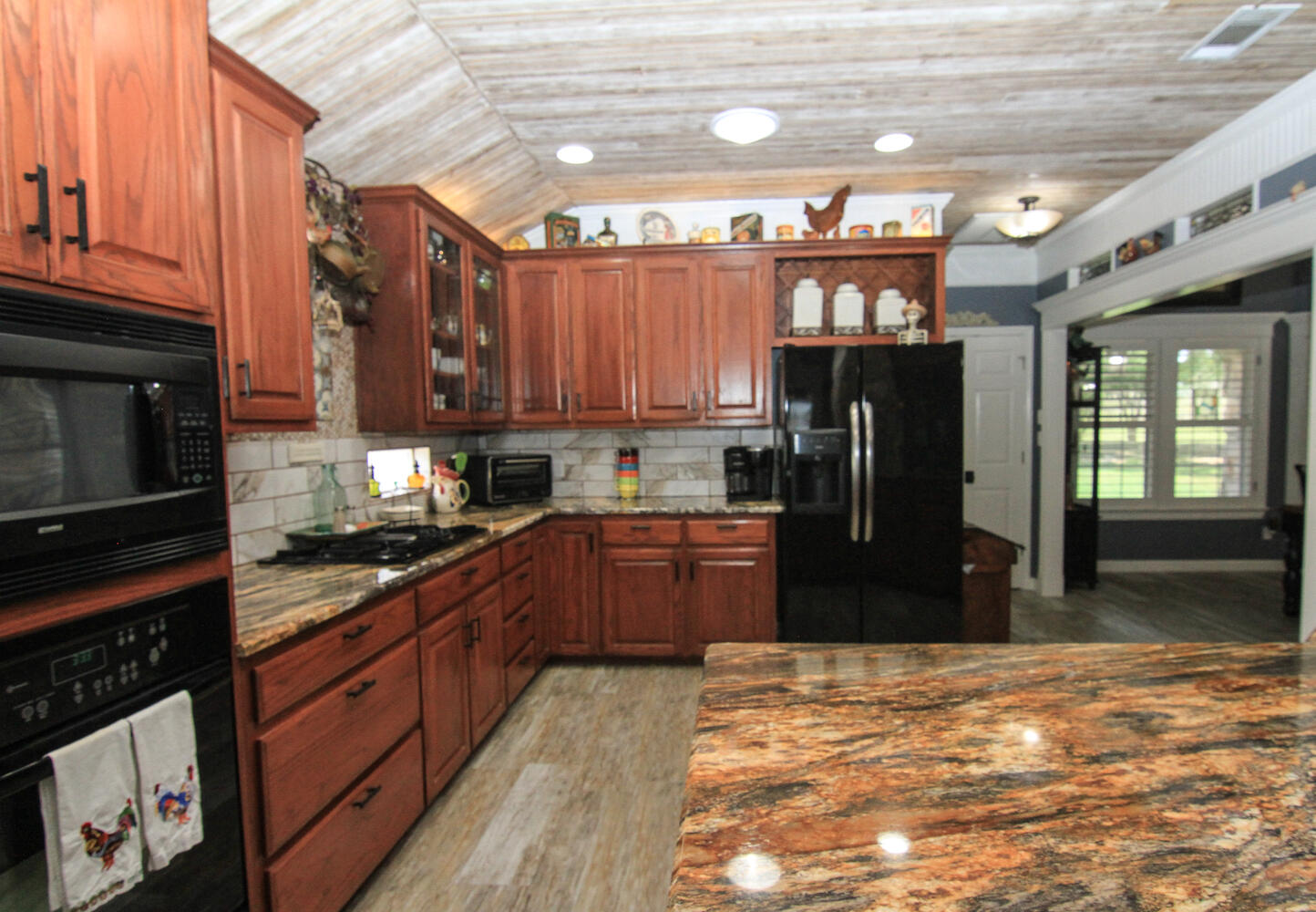 219 Young Ranch Road Georgetown, TX 78633 - Photo 19 of 40 Kitchen featuring black appliances, vaulted ceiling, dark stone countertops, glass insert cabinets, and open to dining and breakfast