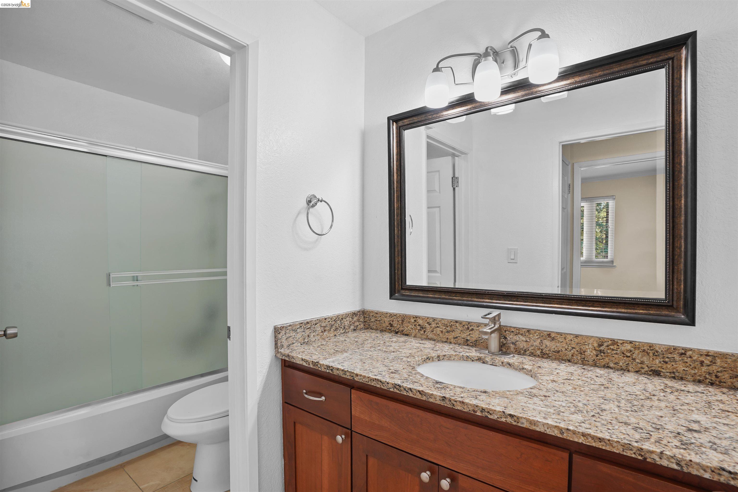 1505 Kirker Pass Road, Unit 214 Concord, CA 94521 - Photo 37 of 55 Bathroom featuring a single vanity with a granite-style countertop, wood-finish cabinetry, and a framed mirror with a three-light fixture