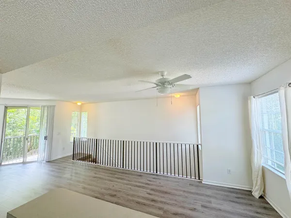 an empty room with wooden floor fan and windows