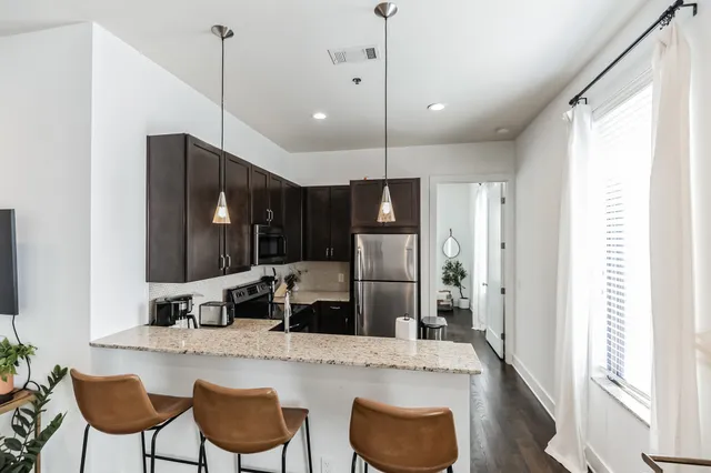 a kitchen with granite countertop a refrigerator a stove a sink and chairs