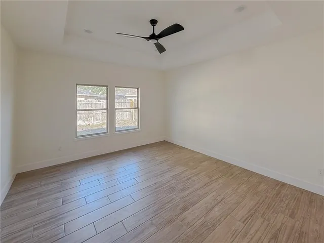 an empty room with wooden floor ceiling fan and windows