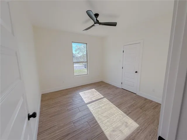 an empty room with wooden floor ceiling fan and windows