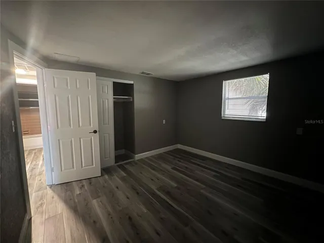 an empty room with wooden floor and windows with curtains