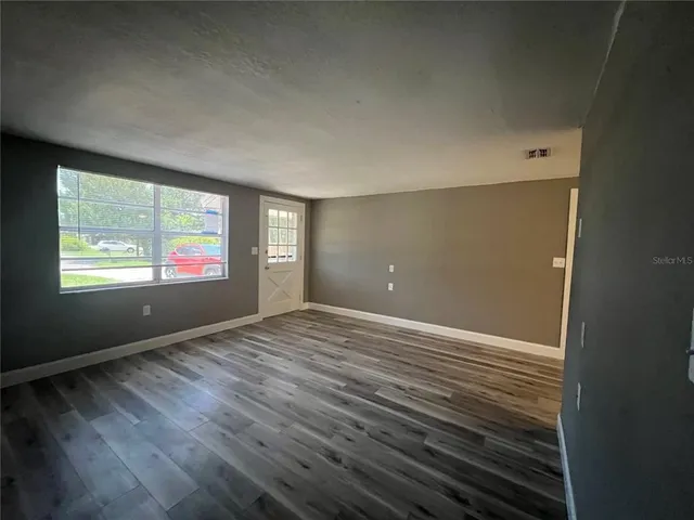 a view of an empty room with wooden floor and a window
