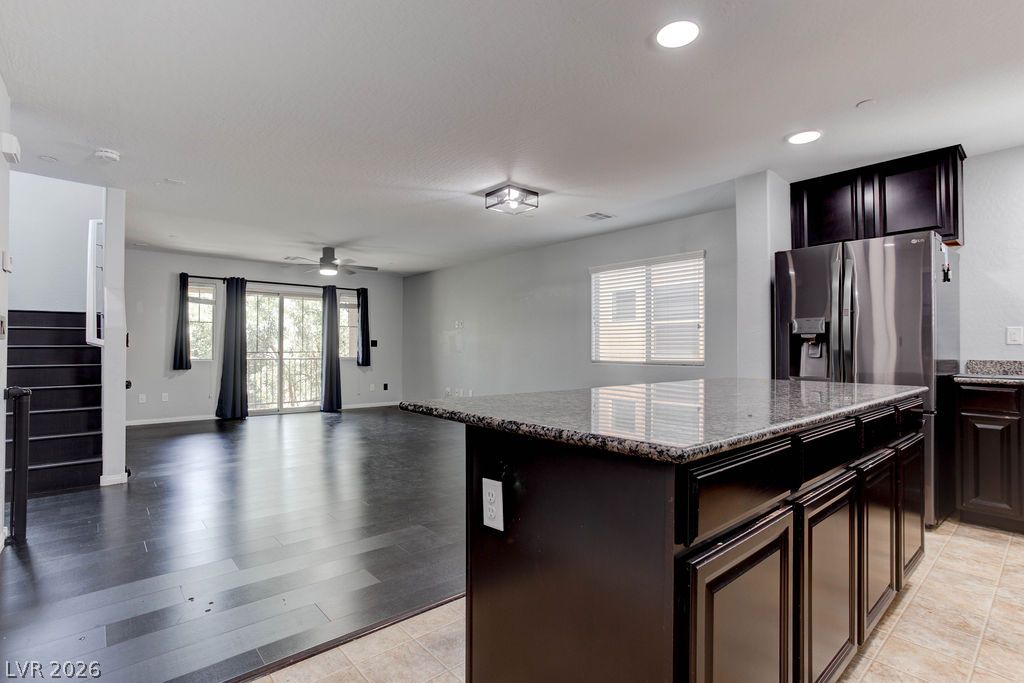 7724 Vibrant Thread Court Las Vegas, NV 89149 - Photo 12 of 43 A sleek kitchen island with granite countertops anchors this contemporary living area featuring dark hardwood flooring.