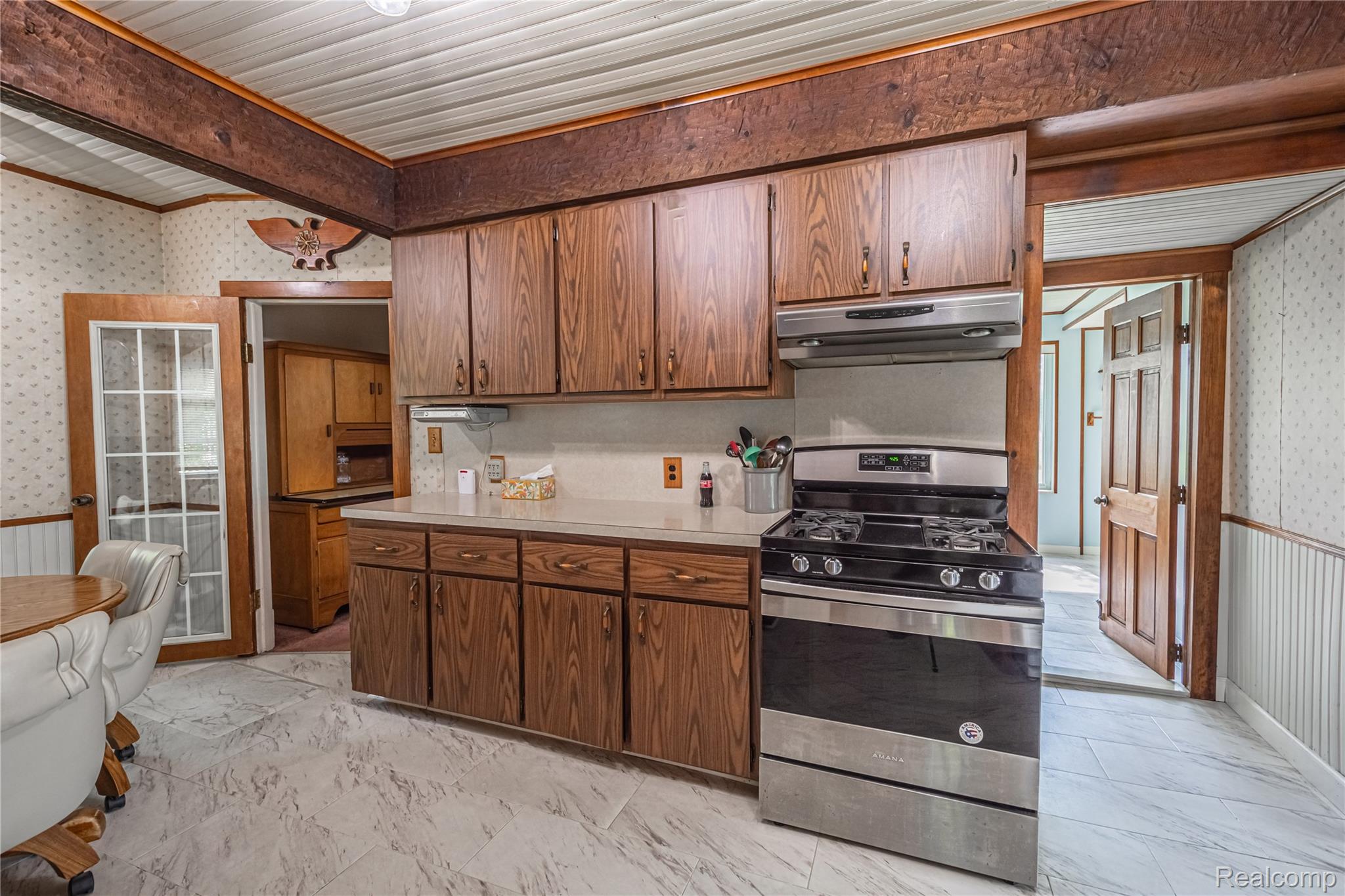 8384 Imlay City Road Avoca, MI 48006 - Photo 27 of 39 Kitchen featuring wood cabinetry, light-toned countertops, a stainless steel gas range with overhead ventilation, and patterned flooring