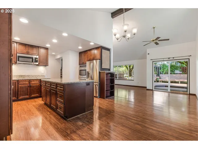 a open kitchen with stainless steel appliances granite countertop a refrigerator a sink dishwasher a oven and a dining table with wooden floor