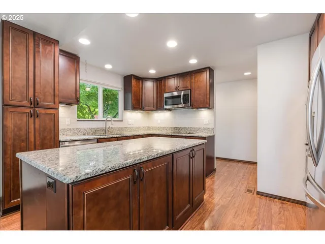 a kitchen with kitchen island granite countertop wooden cabinets a refrigerator and a sink