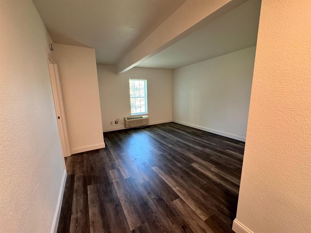 312 West Rentz Street, Unit 99 Weatherford, TX 76086 - Photo 7 of 7 Unfurnished room with a wall unit AC, dark wood-style floors, baseboards, and beamed ceiling