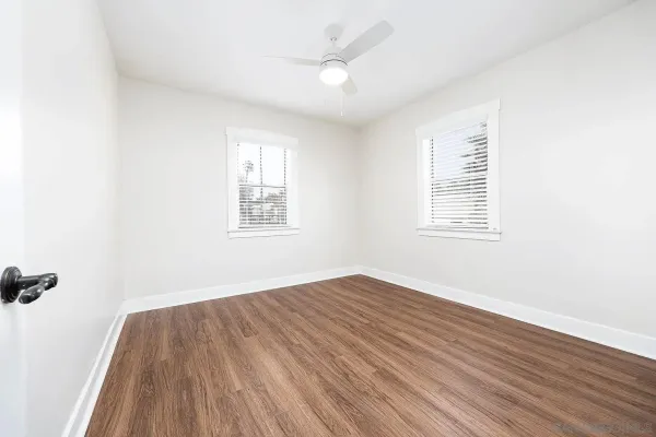 an empty room with wooden floor ceiling fan and windows