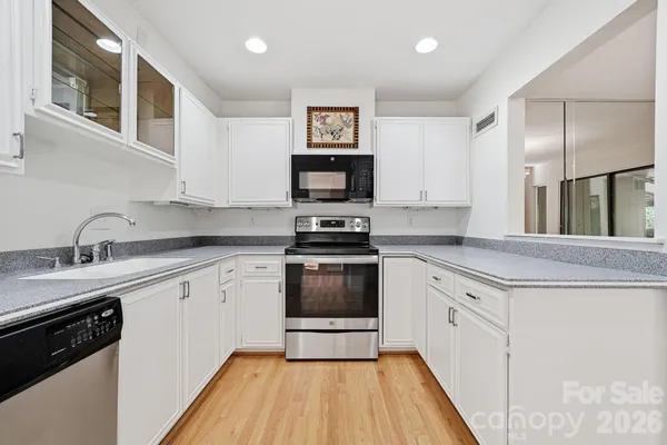 a kitchen with granite countertop a stove top oven a sink dishwasher and white cabinets with wooden floor