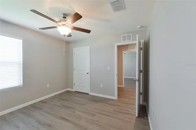 an empty room with wooden floor fan and windows
