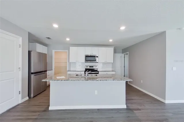 a view of kitchen with stainless steel appliances granite countertop a stove top oven a refrigerator and white cabinets with wooden floor