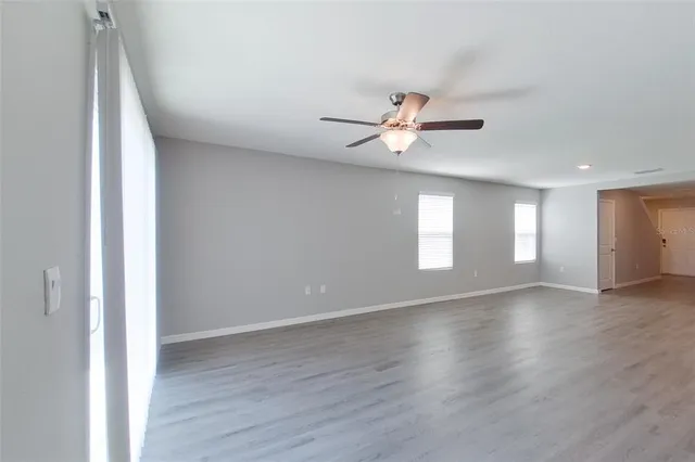 an empty room with wooden floor ceiling fan and window