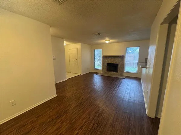 an empty room with wooden floor fireplace and windows