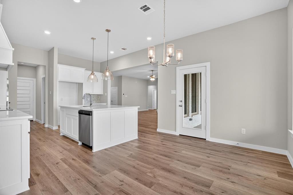 504 Clifton Court Springtown, TX 76082 - Photo 17 of 36 Open-concept kitchen and dining area featuring wood-finish flooring, white cabinetry, a kitchen island with a built-in sink, and pendant lighting