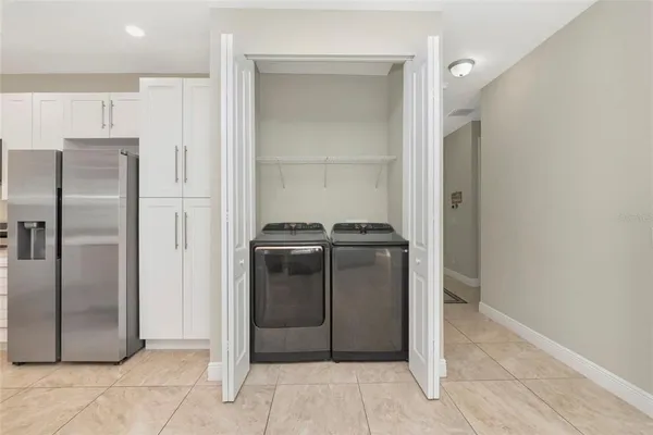 a view of a refrigerator in kitchen and an empty room with wooden floor cabinet