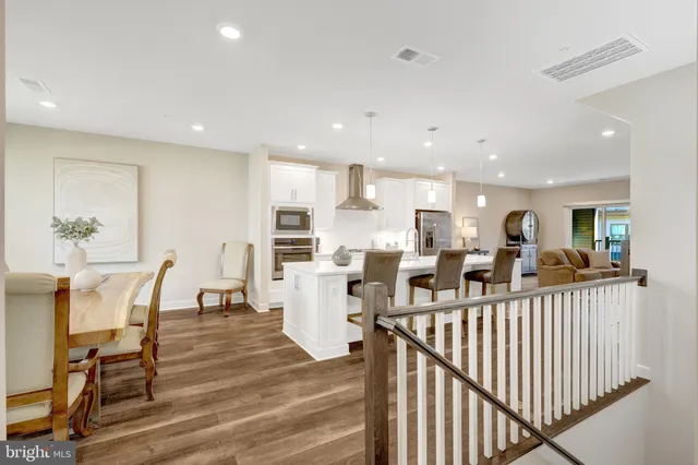 a kitchen with stainless steel appliances kitchen island granite countertop a refrigerator a stove a sink a dining table and chairs with wooden floor