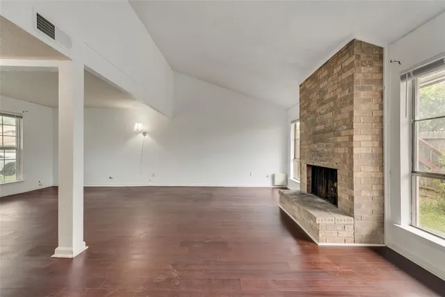 an empty room with wooden floor fireplace and windows