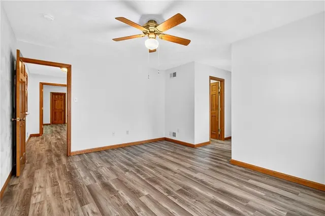 a view of an empty room with wooden floor and a ceiling fan