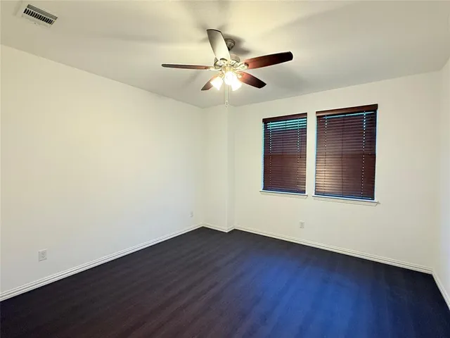 a view of an empty room with wooden floor and a ceiling fan
