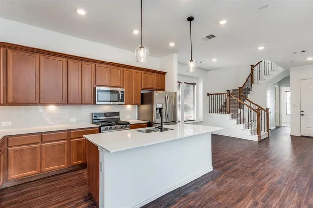 a kitchen with stainless steel appliances kitchen island granite countertop a stove top oven a sink dishwasher a refrigerator and cabinets with wooden floor