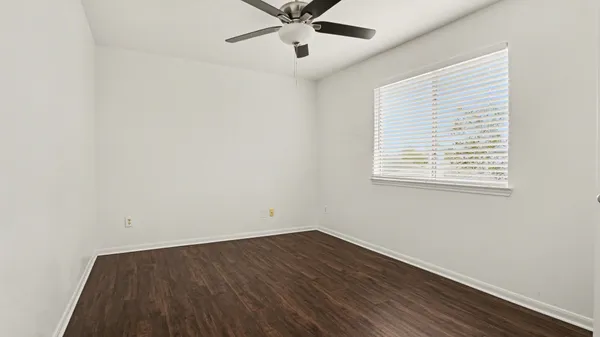an empty room with wooden floor chandelier fan and windows