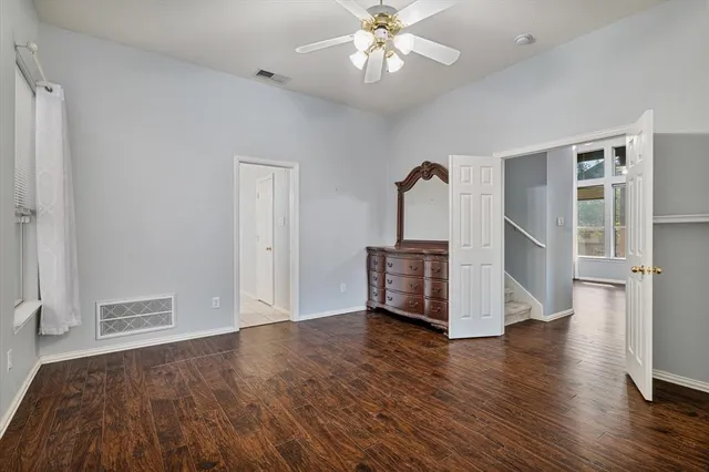 a view of an empty room with wooden floor and a ceiling fan