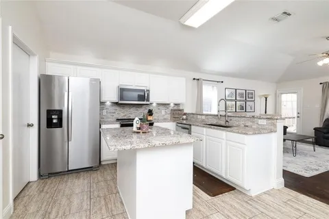 a kitchen with stainless steel appliances a sink a stove a refrigerator cabinets and a dining table