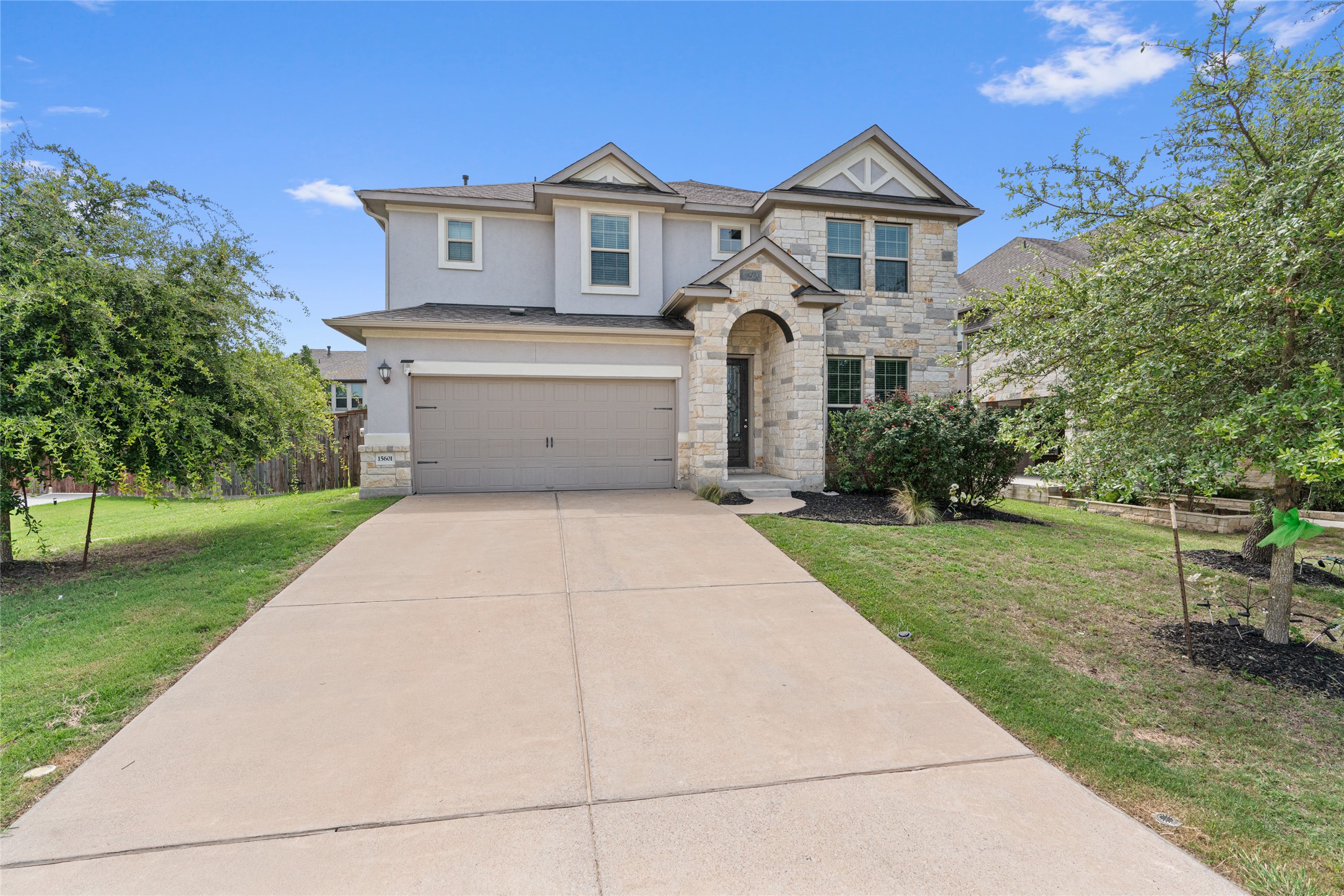 Two-story residence featuring a stone and stucco exterior, an arched entryway, a paved driveway, an attached two-car garage, and established front yard landscaping