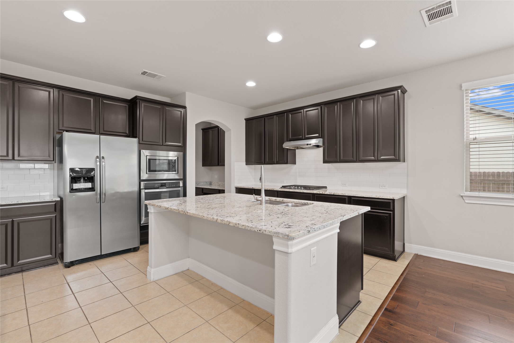 15601 Cabrillo Way Austin, TX 78738 - Photo 11 of 32 Kitchen featuring a granite-topped island with an undermount sink, dark wood cabinetry, stainless steel appliances, a white subway tile backsplash, and recessed lighting